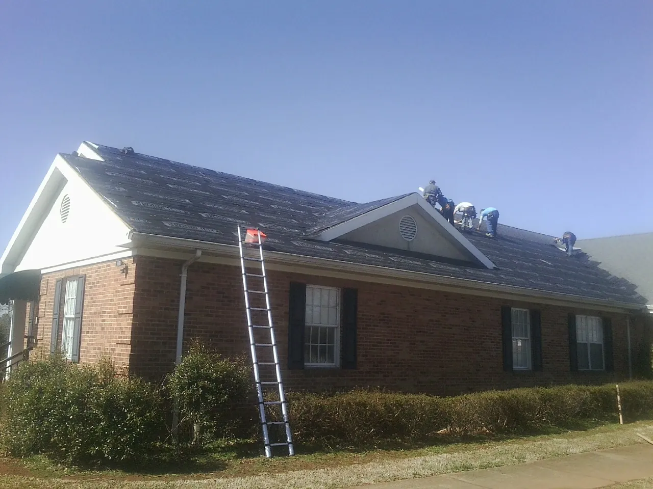Crew tearing shingles off a brick ranch roof with a ladder set — Metal Roof Repair work by our crew in Londonderry