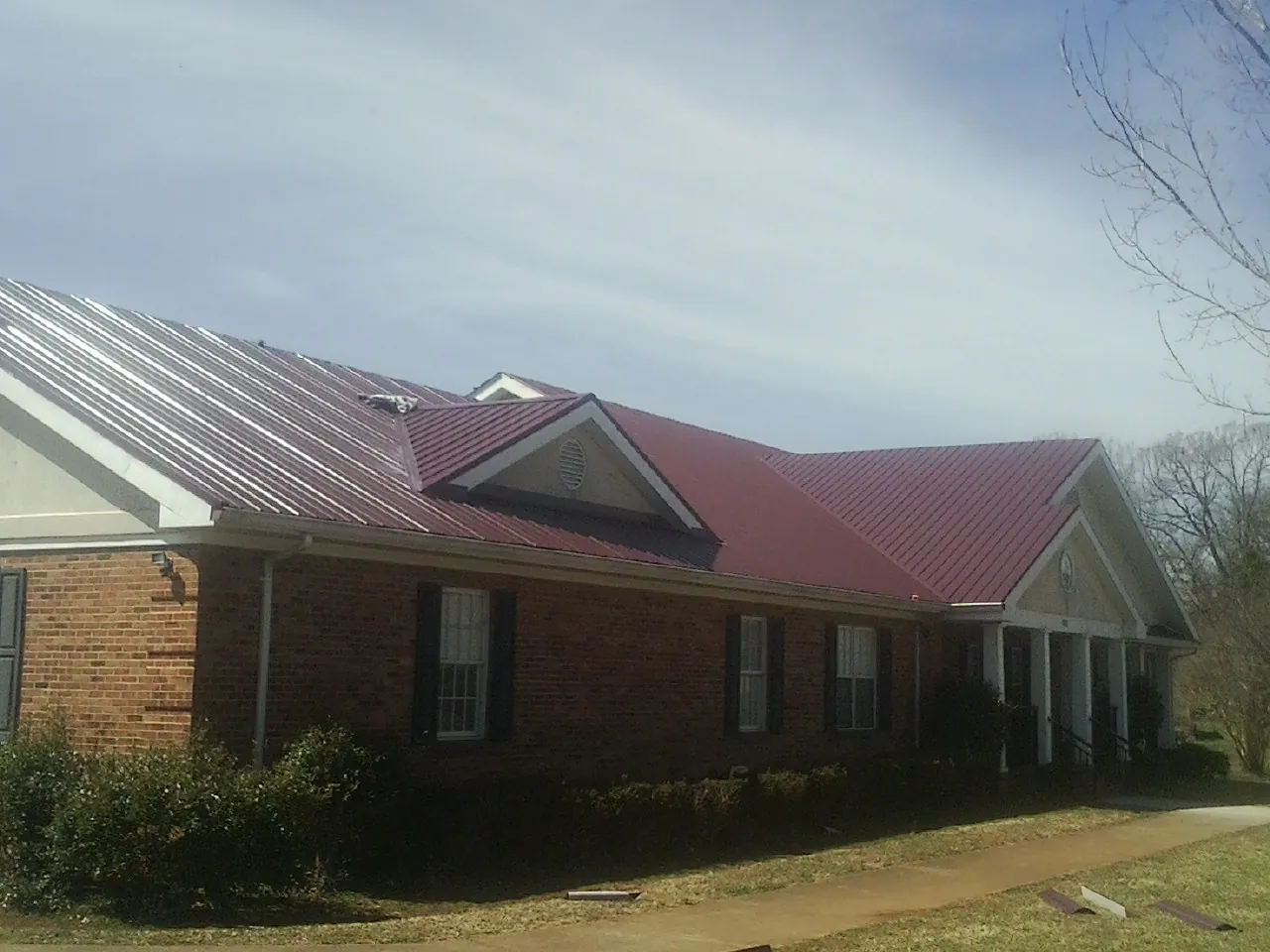 Red metal roof with gabled entries on a long brick building, from a Hail Damage Roof Repair job in Londonderry