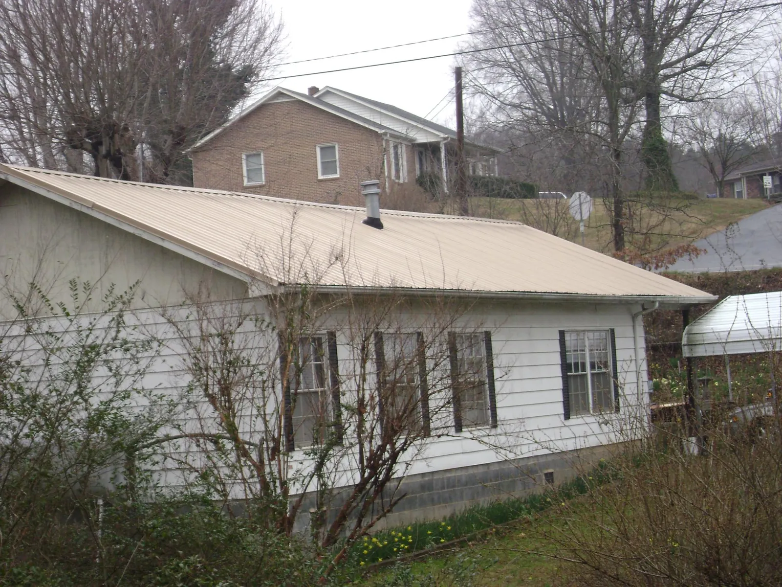 Tan metal roof on a white sided house set into a hillside — Commercial Roofing by Roofing Brothers in Londonderry